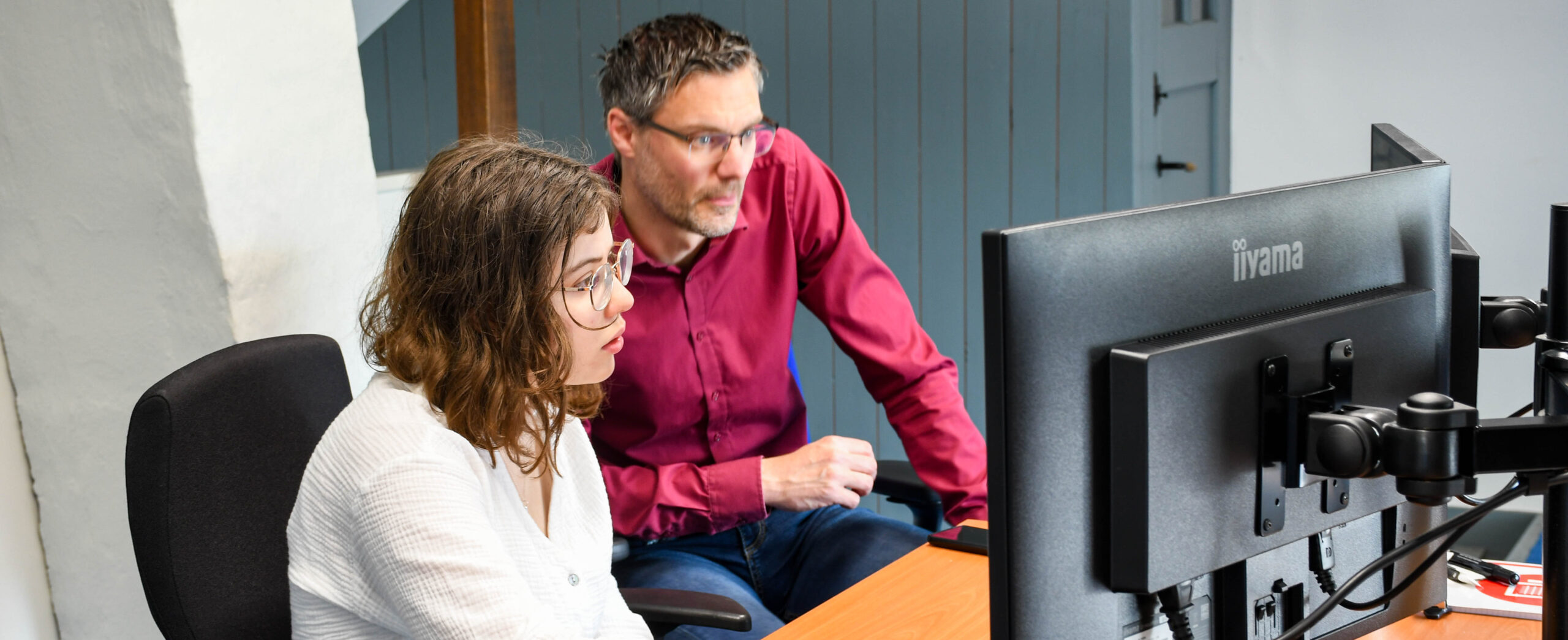 Foto van twee collega's achter een bureau terwijl ze naar een computerscherm kijken.